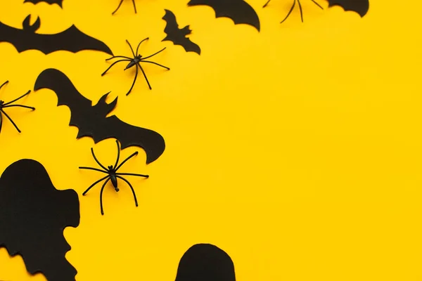 Halloween flat lay. Bats, spiders and ghosts decoration on yellow background. Happy Halloween! Halloween template with space for text. Festive decor border layout