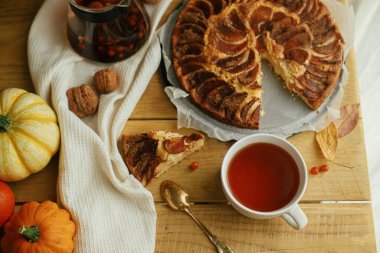 Tarçınlı taze elmalı turta, sonbahar yaprakları, balkabakları ve fındıklı kırsal ahşap masada, şık fincanda sıcak çay. Sonbahar kızarıklığı hala hayat, üst manzara. Atmosferik konforlu ev