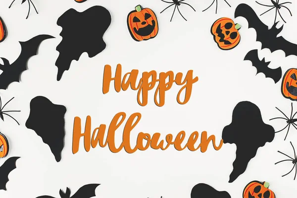Happy Halloween text on black ghosts, spiders, bats and pumpkins on white background flat lay. Happy Halloween! Creative greeting card, handwritten sign. Trick or treat!