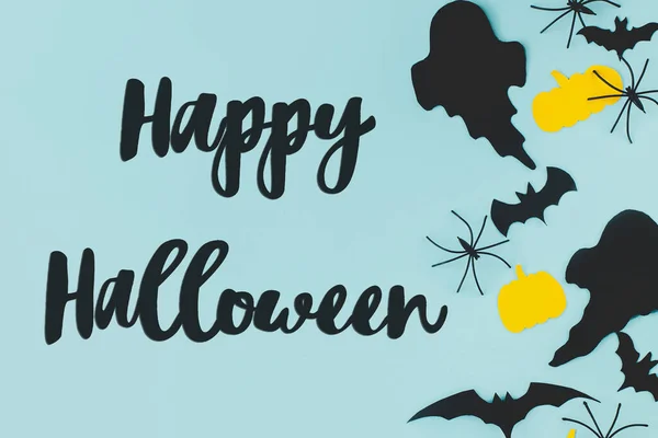 Happy Halloween! Happy Halloween text on black ghosts, spiders, bats and pumpkins on blue background flat lay. Creative greeting card, handwritten sign. Trick or treat!