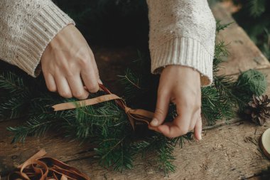 Noel kırsal çelengi yapıyorum. Kırsal ahşap masada kadife kurdele ve çelenk tutan kadın elleri. Huysuz tatil imajı. Kış tatili atölyesi, Noel hazırlıkları
