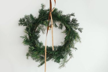 Beyaz arka planda kadife kurdeleli şık bir Noel çelengi ve altın çanlar asılı. Noel kırsal çelengi, karamsar bir görüntü. Kış tatili dekoru. Mutlu Noeller.!