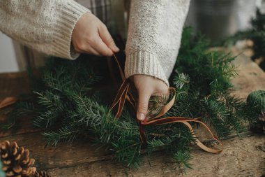 Noel kırsal çelengi yapıyorum. Kırsal ahşap masada kadife kurdele ve çelenk tutan kadın elleri. Huysuz tatil imajı. Kış tatili atölyesi, Noel hazırlıkları