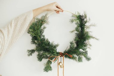 Mutlu Noeller ve mutlu tatiller! El ele tutuşmak modern noel çelengi kadife kurdele ve beyaz arka planda altın çanlar. Kış tatili dekorasyonu, karamsar görüntü