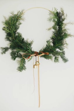 Mutlu Noeller ve mutlu tatiller! Beyaz arka planda kadife kurdeleli ve altın zilli modern Noel çelengi. Kış tatili dekorasyonu, karamsar bir görüntü. Boho çelengi