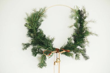 Mutlu Noeller ve mutlu tatiller! Beyaz arka planda kadife kurdeleli ve altın zilli modern Noel çelengi. Kış tatili dekorasyonu, karamsar bir görüntü. Boho çelengi