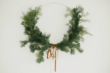 Beyaz arka planda kadife kurdeleli ve altın zilli modern Noel çelengi. Mutlu Noeller ve mutlu tatiller! Kış tatili dekorasyonu, karamsar bir görüntü. Boho çelengi