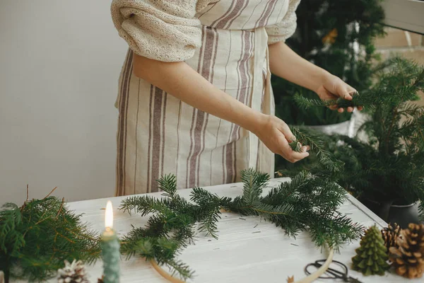 制作现代圣诞花环 女人的手 用冷杉枝在白色的木制桌子上 用蜡烛 彩带在圆圈上做花圈 假日工作坊冬季装饰 喜怒无常的形象 — 图库照片