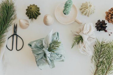 Sıfır atık Noel yatıyordu. Beyaz köy masasında keten kumaşlara sarılmış şık hediyeler. Çevre dostu ahşap oyuncaklar, köknar dalları, mum. Furoshiki hediye paketi. İyi tatiller.!