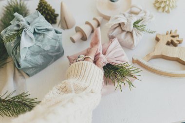 Sıfır boşa geçen Noel. Beyaz masa arka planında köknar dalı olan pembe kumaşa sarılı hediye paketi çevre dostu ahşap dekor ve mum ile birlikte. Furoshiki hediye paketi. Mutlu Noeller.!