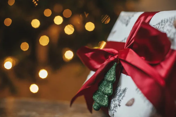 黄金の光とクリスマスツリーでスタイリッシュなクリスマスプレゼント 夜の部屋で赤い弓と光沢のある木の装飾が施されたクリスマスプレゼントを包んだ メリークリスマス 雰囲気バナー テキストのためのスペース — ストック写真