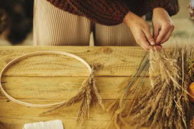 Kırsal masada şık bir sonbahar çelengi yapmak. Elleri çember üzerine kurumuş çim düzenleme tahta masa üzerinde makas, iplik. Çiftlik evinde sonbahar dekorasyonu ve düzenleme.