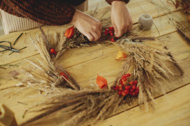 Kırsal masada şık bir sonbahar çelengi yapmak. Kadın elleri böğürtlen, kuru ot, tahta masada çelenk. Çiftlik evinde sonbahar dekorasyonu ve düzenleme