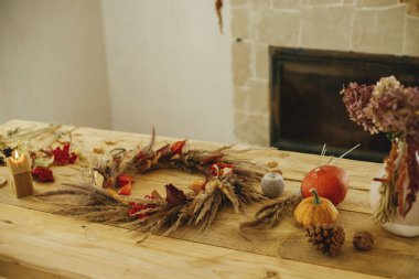 Çiftlik evinde sonbahar dekorasyonu ve düzenleme. Çelenk, mum, kurumuş çimen, iplik, balkabağı ve mum. Şöminenin kırsal masasında şık bir sonbahar çelengi yapmak.