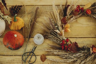 Kırsal masa üzerinde şık bir sonbahar çelengi. Çiftlik evinde sonbahar dekorasyonu ve düzenleme. Kurumuş çimen, böğürtlen, ahşap masa üzerinde kabak ve makaslı kırsal sonbahar çelengi..