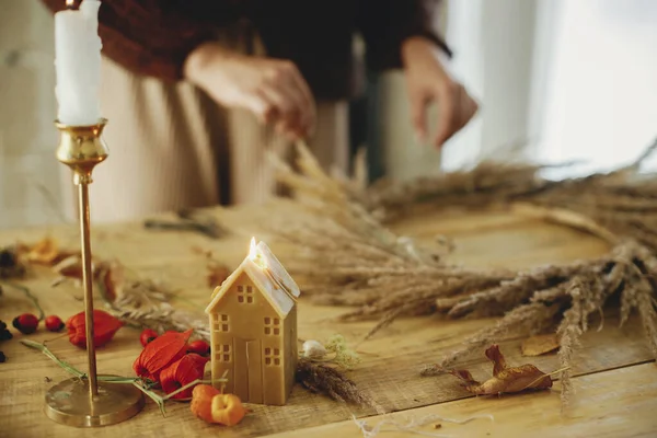 女性双手在木制桌子上的花圈中摆放干草的背景上 点缀着时尚的蜡烛 在乡村餐桌上做时尚的秋天花环 农舍的秋季装修和布置 — 图库照片