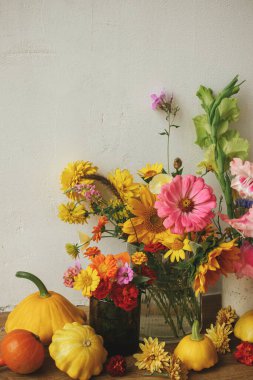 Autumn rustic still life. Colorful autumn flowers, pumpkins, pattypan squashes composition against rustic wall. Harvest in countryside. Happy Thanksgiving! Hello Fall, moody atmospheric image