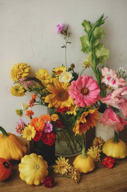 Autumn rustic still life. Colorful autumn flowers, pumpkins, pattypan squashes composition against rustic wall. Harvest in countryside. Happy Thanksgiving! Hello Fall, moody atmospheric image
