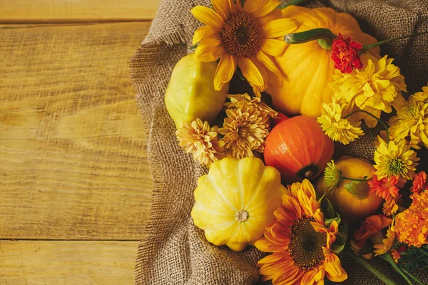 Happy Thanksgiving! Colorful autumn flowers, pumpkins, pattypan squashes on burlap on wooden table. Rustic autumn flat lay, space for text. Seasons greeting card. Harvest time in countryside