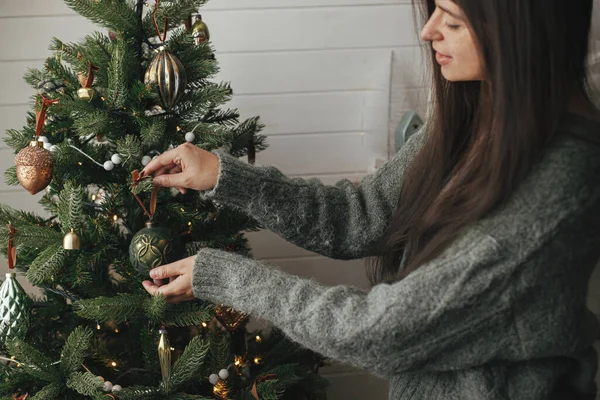 时尚的女人穿着舒适的毛衣 装饰着圣诞树 在大气的节日房间里穿着时髦的便服 圣诞快乐 准备寒假 用老式玩具装饰圣诞树 — 图库照片