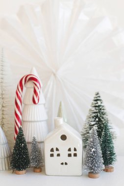 Beyaz masa üzerinde şık küçük Noel ağaçları, evler ve baston şekerler. Mutlu Noeller ve mutlu tatiller! Modern festival sahnesi, minyatür karlı köy. Kış bayrağı, İskandinav dekoru
