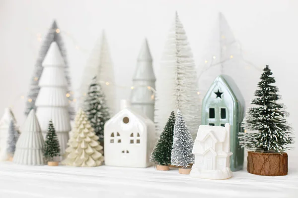 現代のクリスマスシーン 白いテーブルの上にミニチュアの雪の村 メリークリスマス スタイリッシュな小さなクリスマスツリーと家の装飾 冬の休日のバナー スキャンディナヴィアのモノクローム装飾 — ストック写真