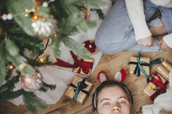 贈り物 トップビューでスタイリッシュなクリスマスツリーの下で所有者と遊ぶかわいい幸せな犬 ペットと冬の休日 お祝いの部屋でトナカイの角で愛らしいデンマークのスピッツ犬と男 メリークリスマス — ストック写真