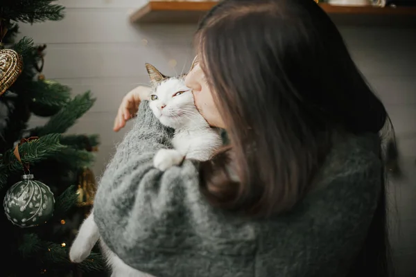 メリークリスマス スタイリッシュなクリスマスツリーの近くで ヴィンテージのベビールでかわいい猫を抱きしめる居心地の良いセーターの女性 ペットと冬の休日 愛らしいです子猫と幸せな女性手コキでお祝い部屋 — ストック写真