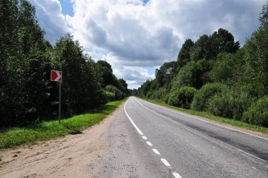 Yol tabelası olan terk edilmiş bir yol manzarası. Yol boyunca gök gürültülü bulutlar.