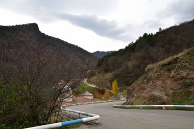 Dağ yolu ve evler boyunca dik iniş manzarası. Yol metal tamponlarla çevrili..