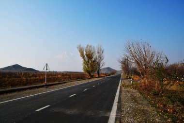 Bir asfalt yol ve Ararat Dağı 'nın zirvelerinin manzarası. Bulutsuz mavi gökyüzü.