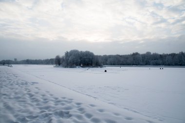 Kış. Donmuş göl manzarası. Buzdaki balıkçılar balık tutuyor..