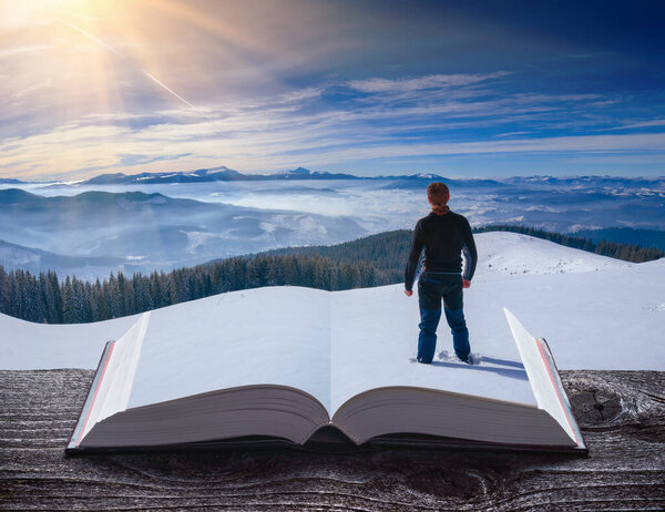 Hiker in a winter mountain valley on a pages of an open book. Winter time. Travel and education concept.