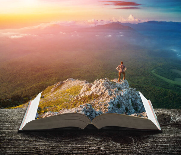 Young active hiker man on a cliff on the pages of an open magical book. Majestic landscape. Travel and education concept.