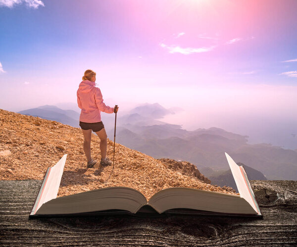 Girl hiker in a rocky mountain top on the pages of an open magical book. Majestic landscape. Travel and education concept.