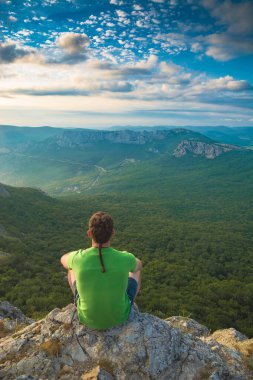 Erkek turist çıplak kayaya oturur. Dağ vadisinin yukarısına bak. Seyahat kavramı.
