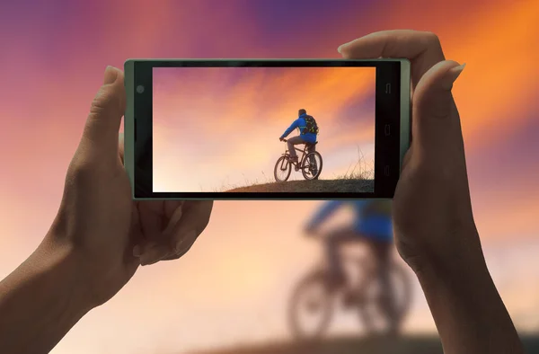 Ciclista Topo Montanha Contra Nuvens Coloridas Uma Tela Smartphone Mãos — Fotografia de Stock