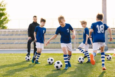 Genç Koç 'la Arkadaşların Futbol Antrenmanı. Okul çocukları çim tarlasında top tekmeliyor. Genç Futbolcular Antrenman Oturumunda Futbol Yeteneklerini Geliştiriyor