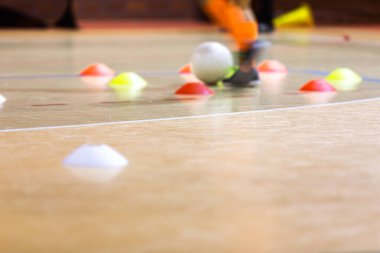 Beyaz futsal topuyla iç saha futbolcusu eğitimi. Futsal idman dribbling talimi. Kapalı spor salonu. Futbolcu ligi. Kapalı alan futbolcusu, top, futsal zemin ve kırmızı koni. Spor geçmişi