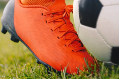 Futbol tekmesi anı. Futbol Cleat ve Futbol Topu 'na yakın çekim. Green Grass Pitch 'te futbolcu tekme topu. Bağlı Red Soccer Kramponları. Spor Futbolu Moda Kıyafetleri