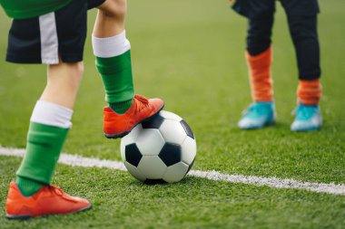 Futbolcu bacaklarındaki görüntüyü klasik topla kapat. Futbol sahasının arka planı ve oyundaki oyuncular. Spor ayakkabılı çocuk saha kenarında topa vuruyor.