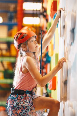 Kapalı alan tırmanma duvarındaki neşeli kız. Kasklı çocuk kaya duvarında eğleniyor. Çocuk tırmanma dersinde öğreniyor. Aile sporu, sağlıklı yaşam tarzı, mutlu aile.. 