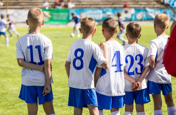 一群穿着球衣的男孩站在足球场的边线上 足球运动员的数量在背上 足球代替队员准备比赛 — 图库照片