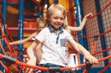 Happy siblings playing together at an amusement park. Excited kids playing together on net ropes. Cute school kids playing on the colorful playground at a shopping mall