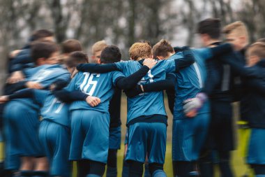 Sahada tezahürat yapan motive olmuş bir genç futbol takımı. Oyuncular sahada bir çember oluşturuyorlar. Koç bir grup futbolcuyla konuşuyor. Antrenörleriyle mutlu futbol takımı 