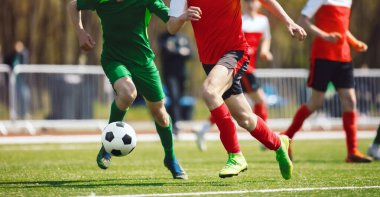 Futbolcular düelloda top oynuyorlar. Yetişkin futbolcular yarışma oyununda. Sporcular çim sahada futbol topunu tekmeliyor