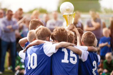 Happy Kids in a Team Rising Golden Trophy During Tournament Celetration. Summer Soccer Competition For Young Boys. Children in Blue Jersey Shirts in a Team Circle clipart