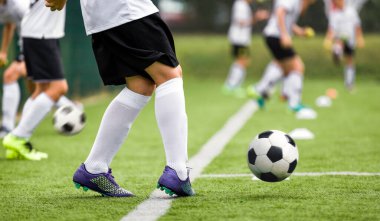 Beyazlı ve siyahlı futbol oyuncusu. Genç atlet çimen tarlasında topa vuruyor. Beyaz Futbol Formalı Tekme Topu 'ndaki çocuk. Çocuklar için Futbol Eğitimi
