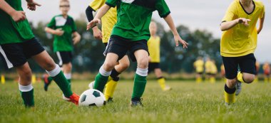 Okul çocukları için futbol yaz kampı. Futbolcular Doğal Çim Sahasında Klasik Futbol Topu koşuyor. Yeşil ve Sarı Futbol Üniformalı Çocuklar Maç Oynuyor