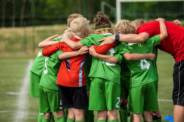 若いコーチと幸せなスポーツチーム スタジアムのピッチでサッカーの試合をする子供たち プレゲームの説明会中に若い選手をやる気トレーナー 緑のサッカージャージの制服の男の子 — ストック写真